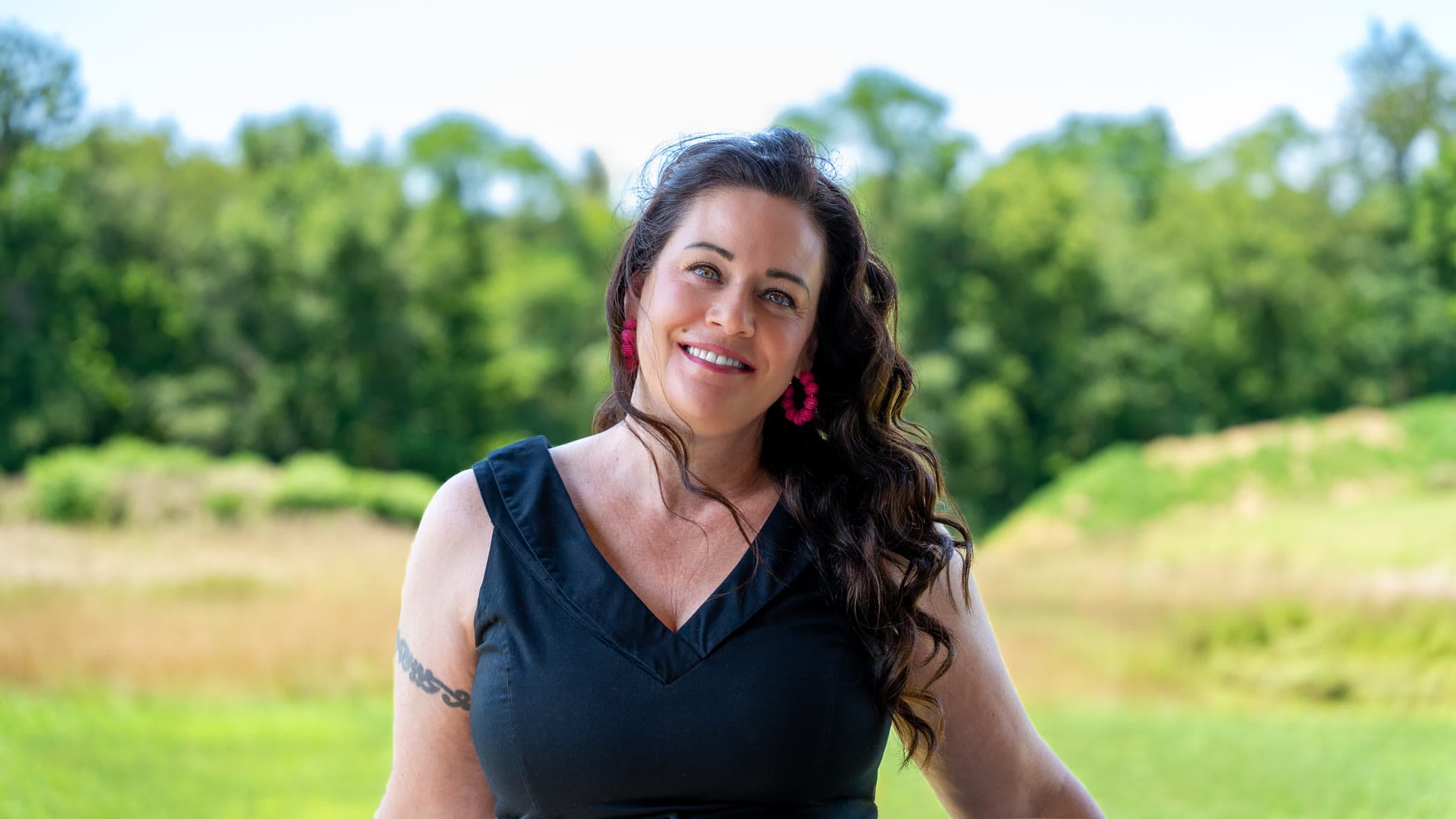 Shannon Clayton smiling outdoors, with a meadow and a line of trees behind her
