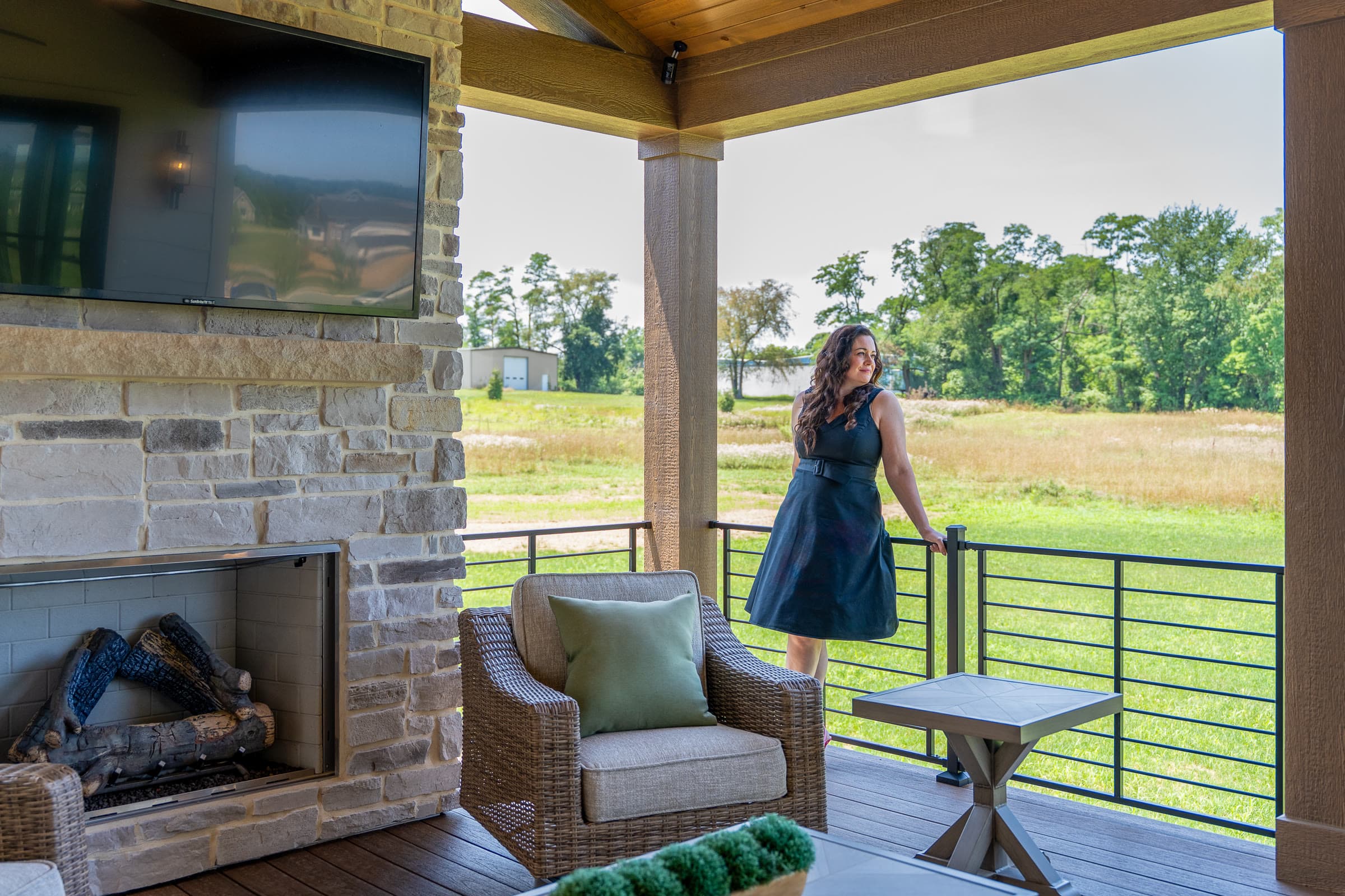Shannon Clayton at the railing of a covered porch with a stone fireplace, looking out over a meadow
