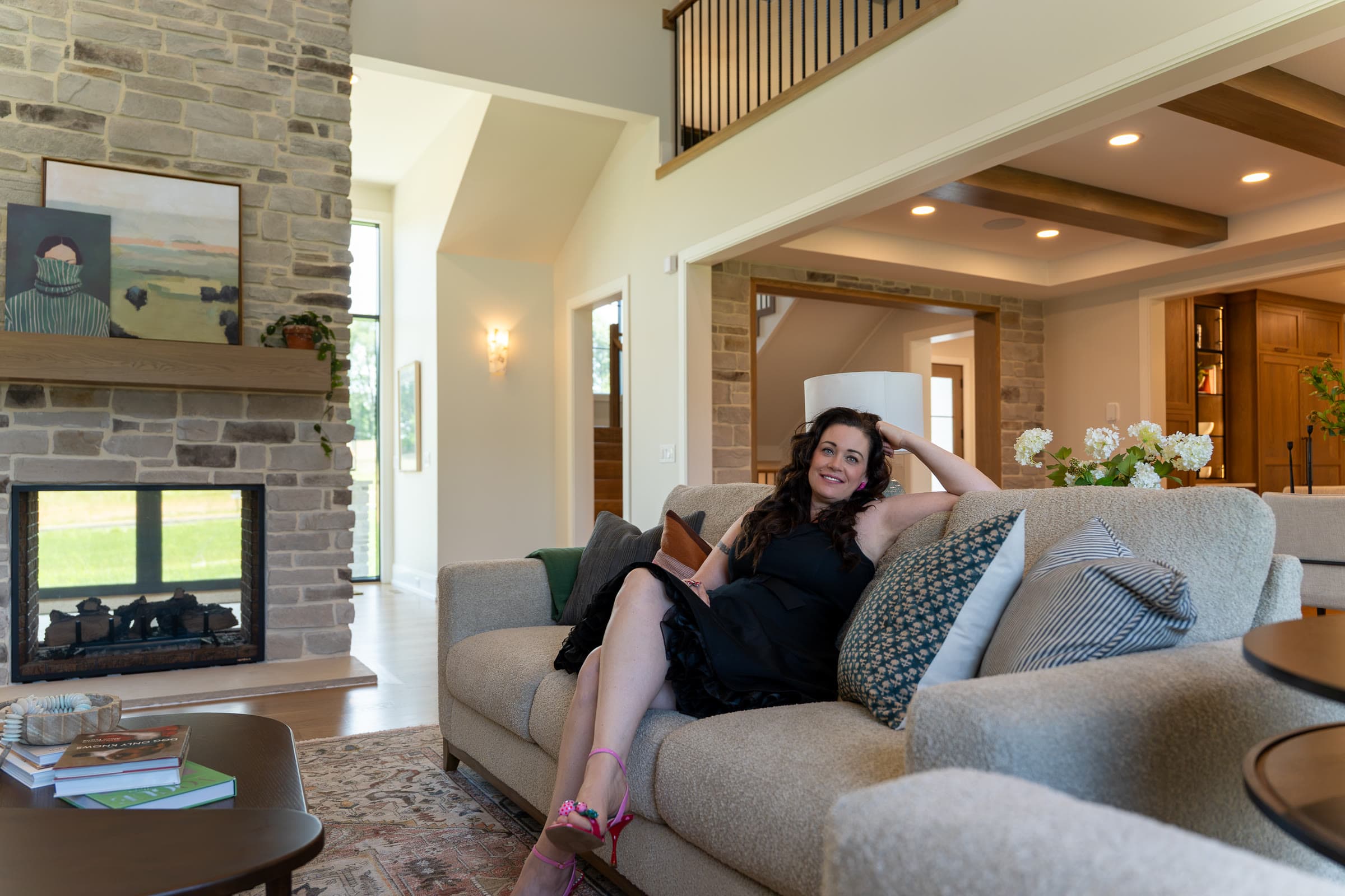 Shannon Clayton seated on a sofa in a living room with a stone fireplace and an open balcony above