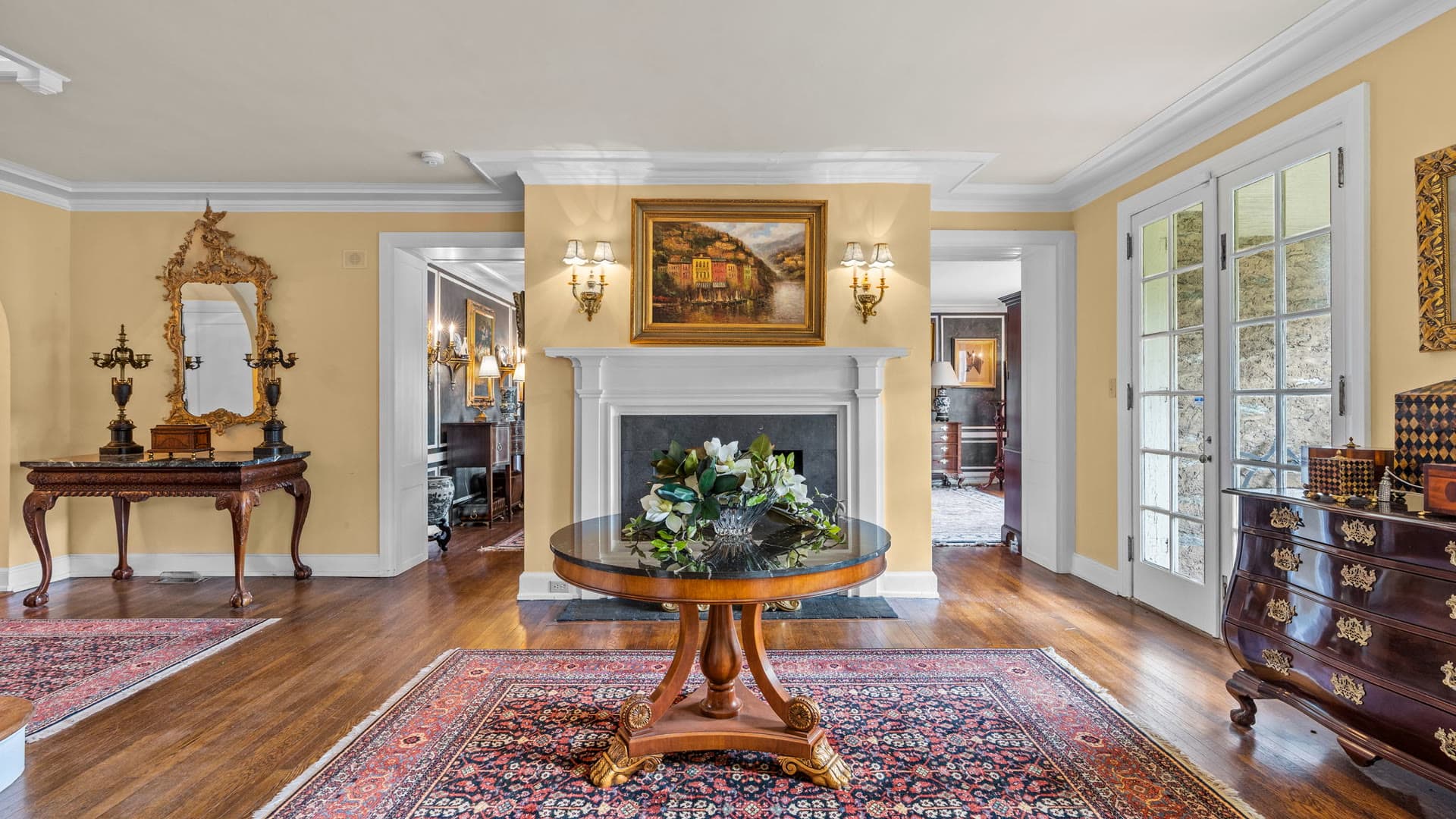 An entry hall with a round pedestal table, oriental rug, and a fireplace beyond