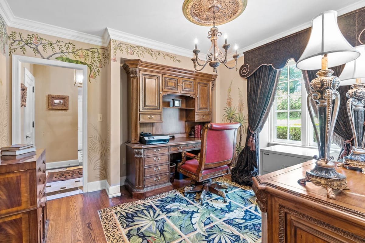 A study with a carved wood desk, a red leather chair, and vines painted on the walls