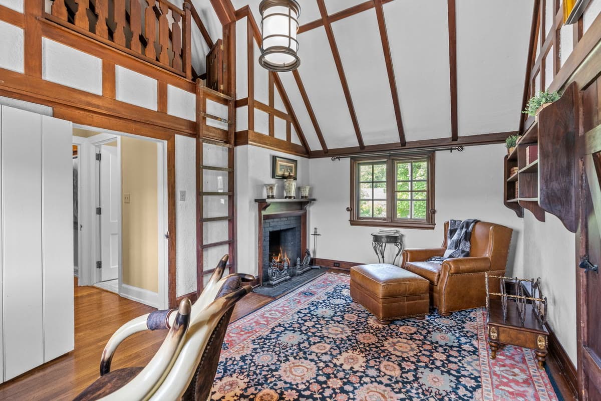 A timber framed room with a loft ladder, a fireplace, and a leather armchair on an oriental rug