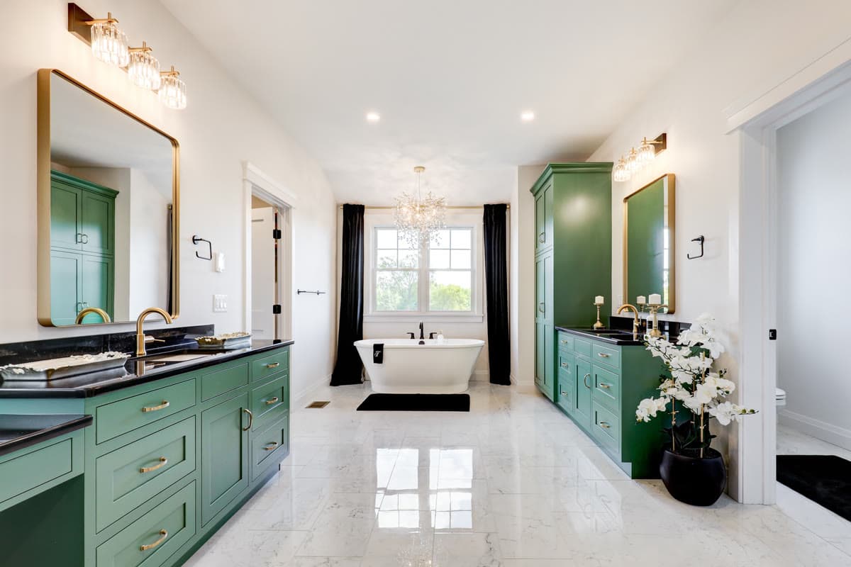 A primary bath with green vanities, brass fittings, and a freestanding tub under the window