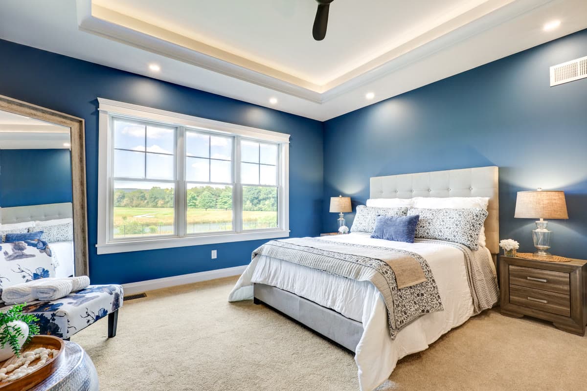 A bedroom with deep blue walls, a tray ceiling, and an upholstered bed