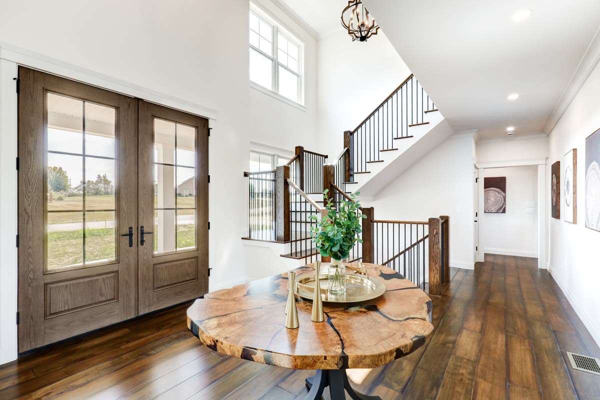 A two storey foyer with a live edge table, double wood doors, and a staircase with iron balusters