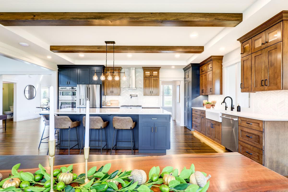 A kitchen with a navy island, timber beams, and walnut cabinetry