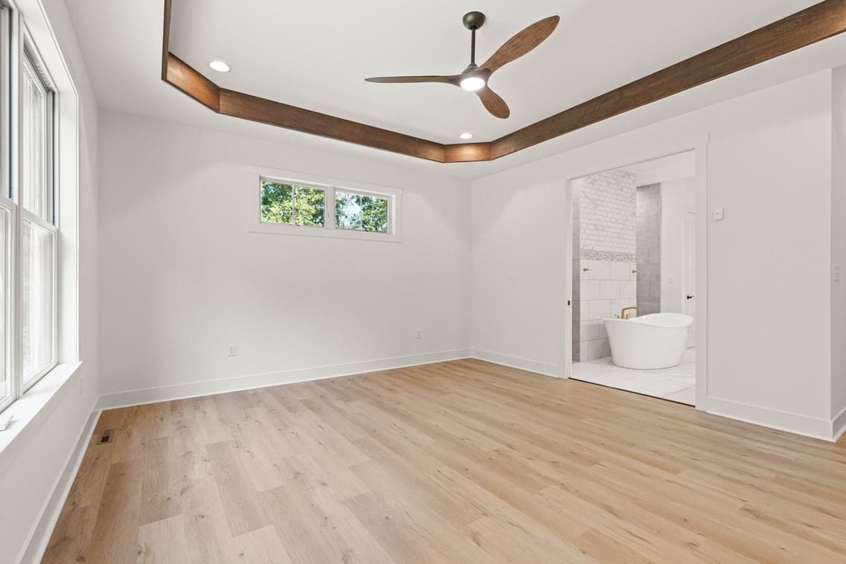 A bedroom with a timber trimmed tray ceiling, opening onto the primary bath