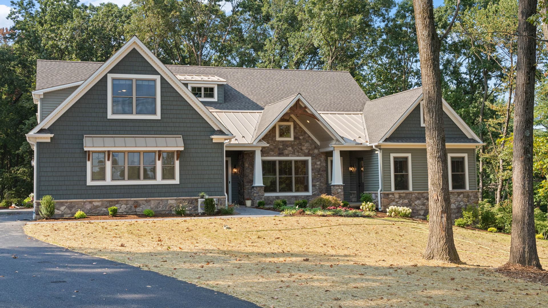 A craftsman house in green siding and stone, set among mature trees