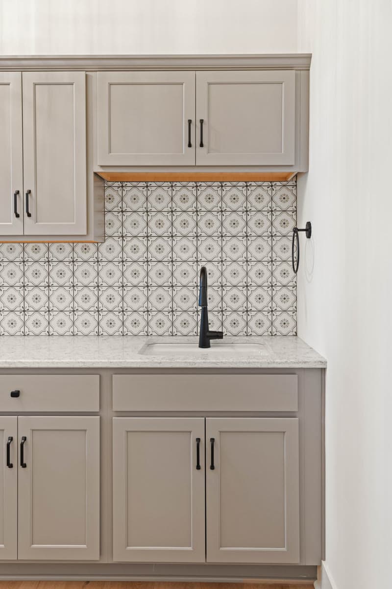 A taupe cabinet and sink with a patterned tile backsplash